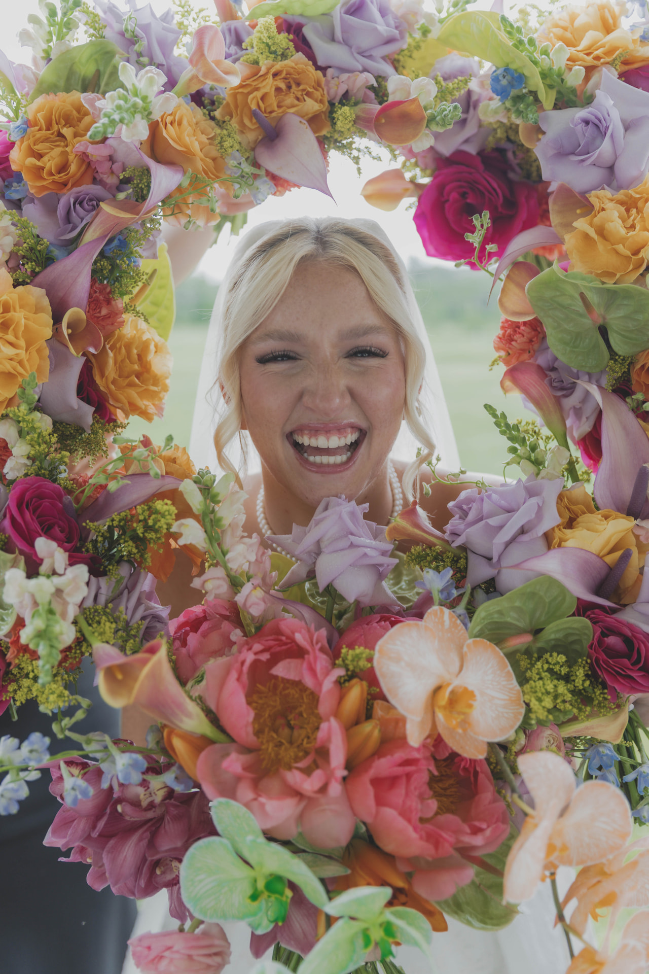Bride laughing framed by vivid pink, orange and lavender wedding florals in mid-Missouri