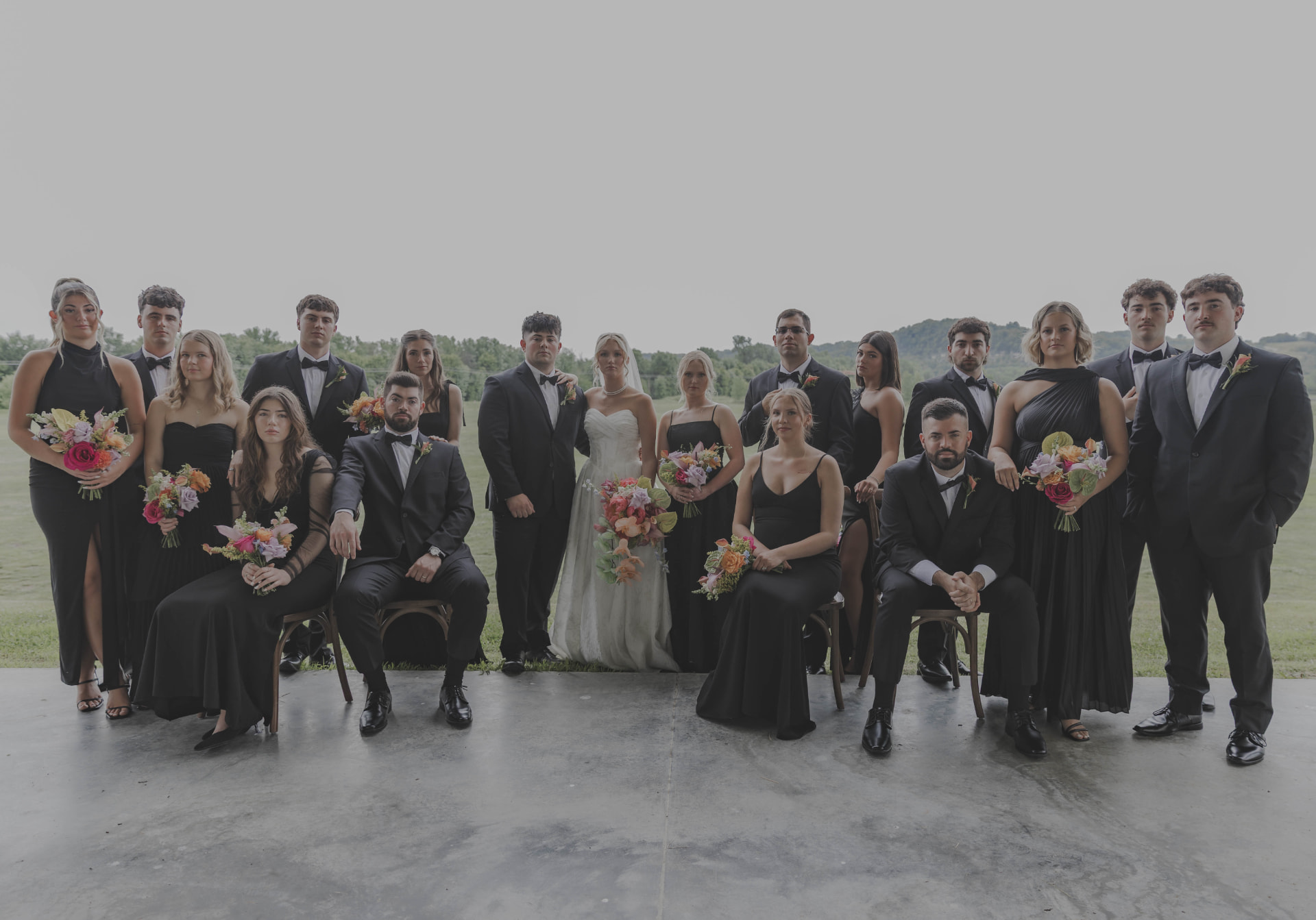 Full wedding party in black formalwear posed across an open lawn at a Columbia, Missouri wedding
