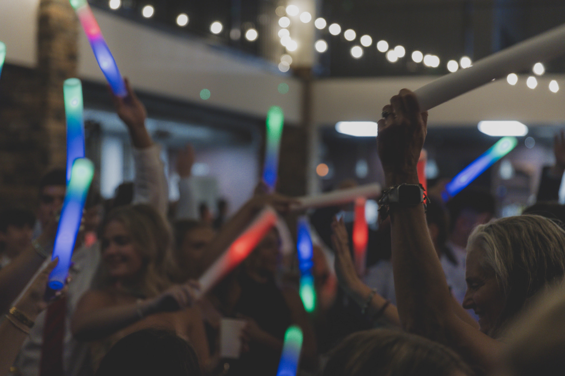 Wedding guests raising glow sticks under string lights at a Columbia MO reception