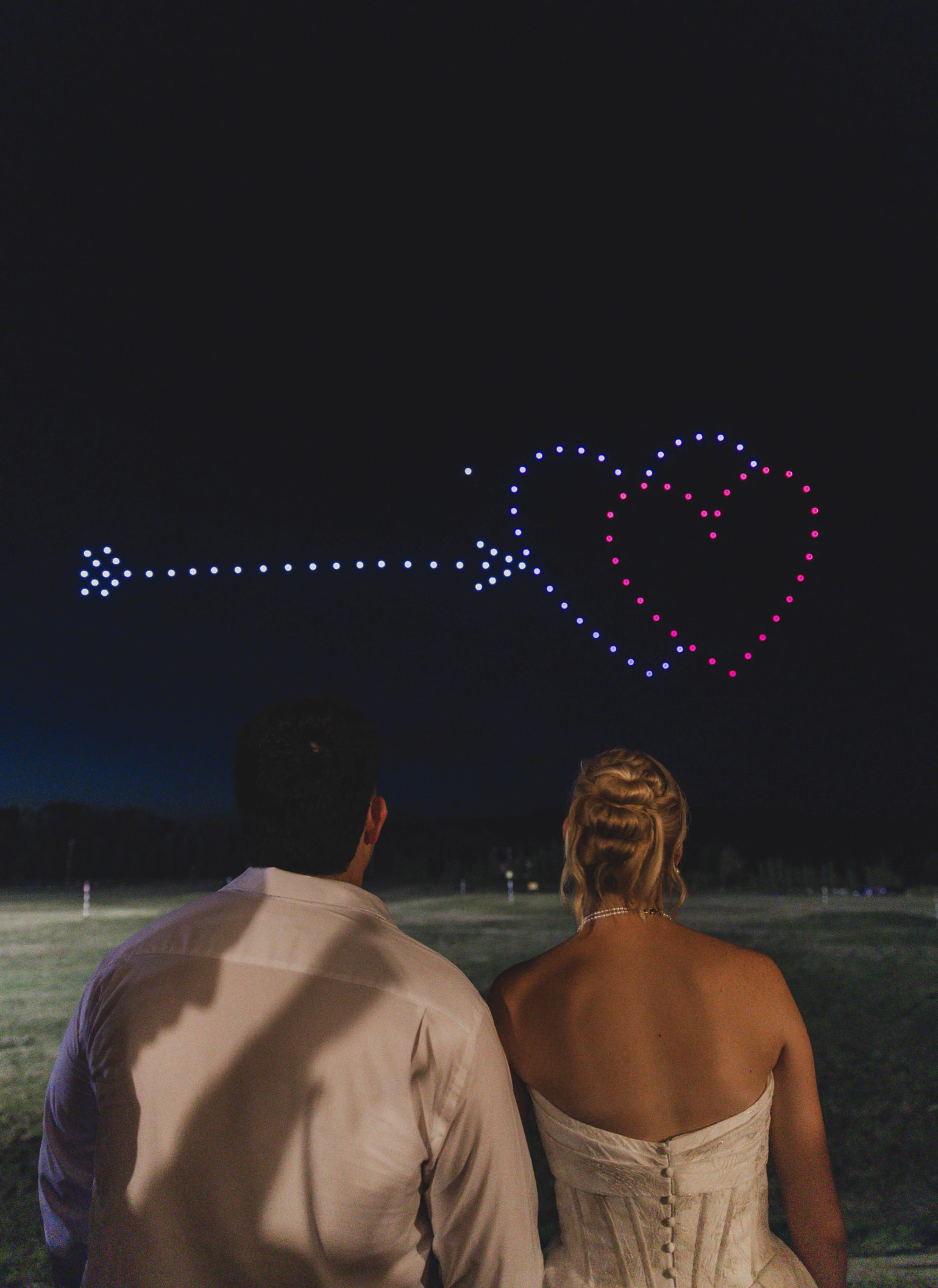 Bride and groom watching a drone light show form a heart in the night sky at a Missouri wedding