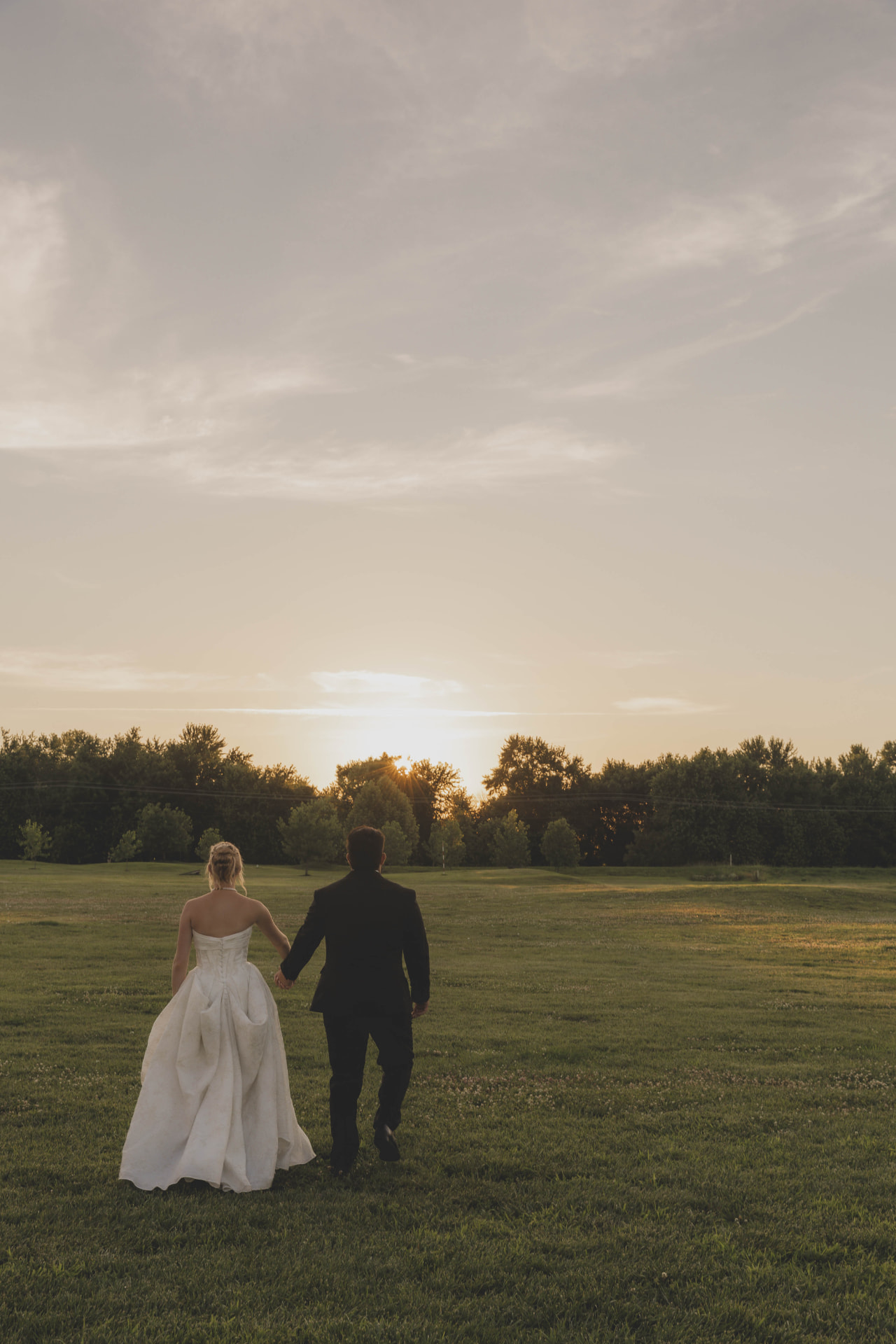 Newlyweds walking toward the sunset across an open Missouri field