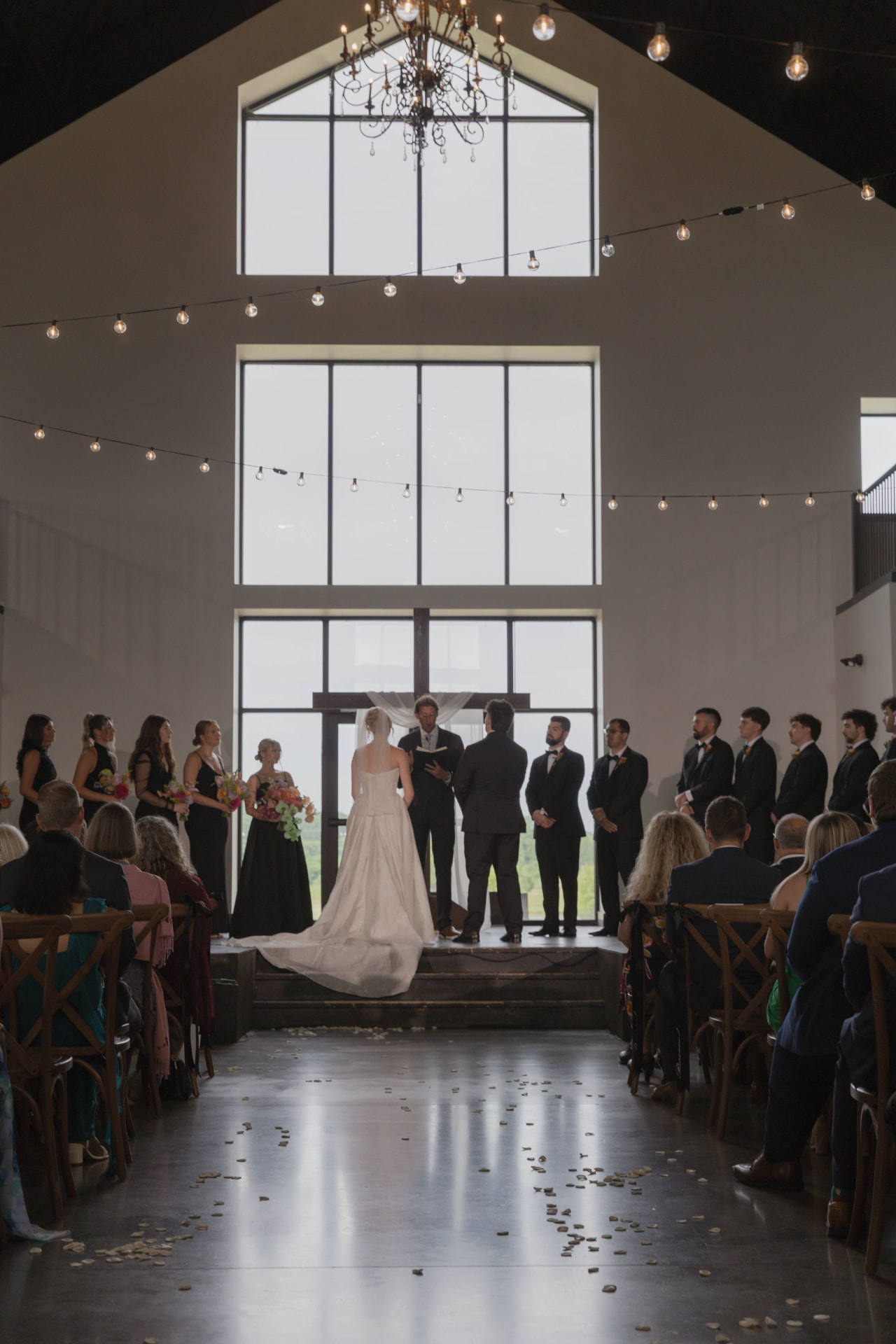 Wide view of a barn wedding ceremony with soaring windows and string lights near Columbia, Missouri