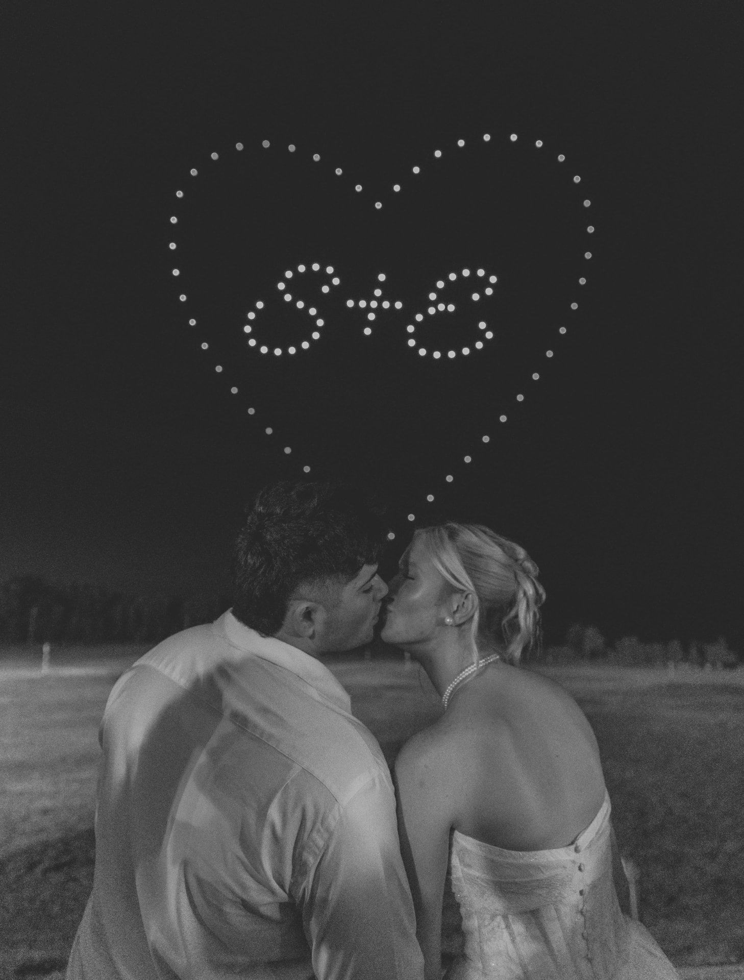 Couple kissing beneath a drone light show heart with their initials at a mid-Missouri wedding send-off