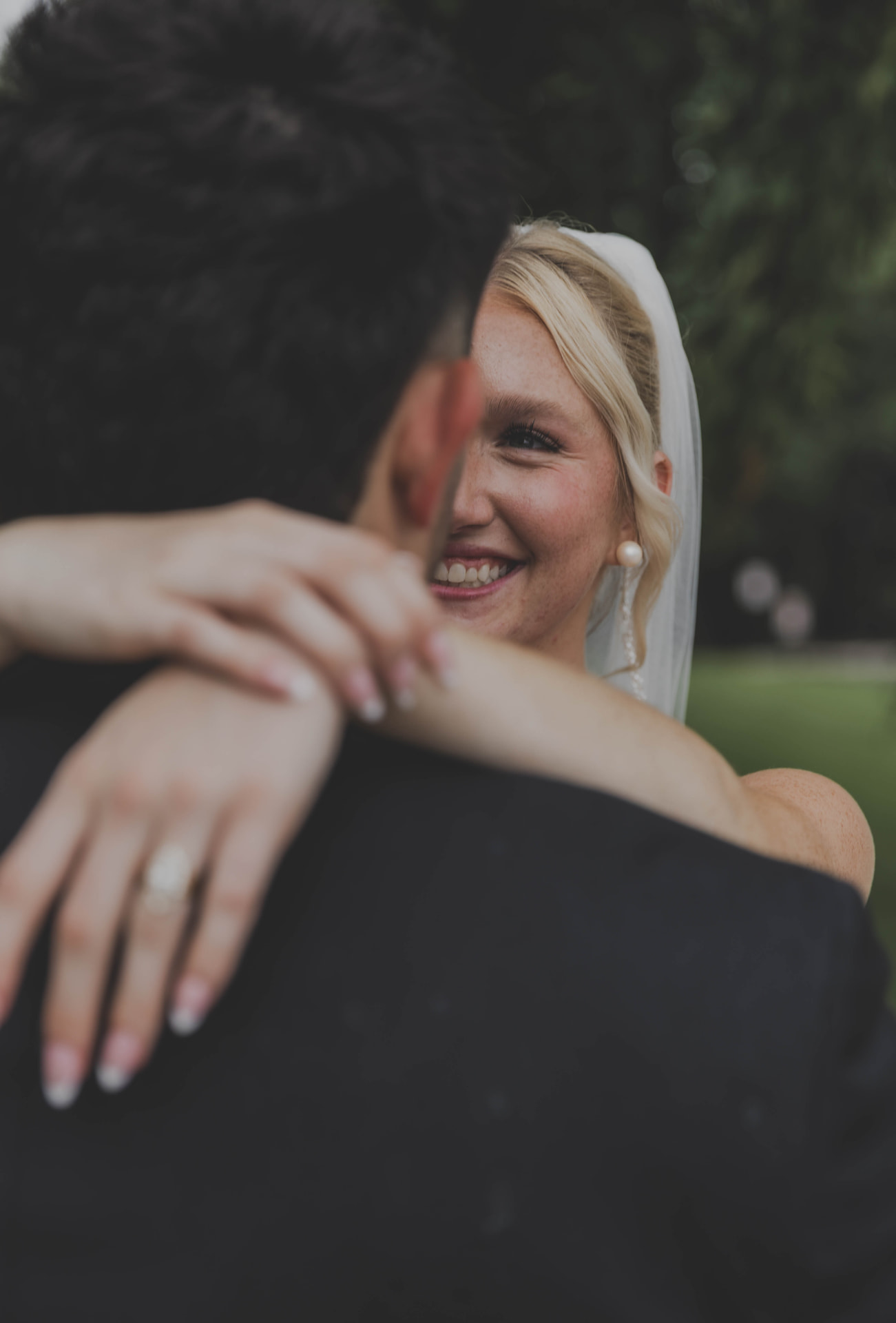 Bride smiling over her husband's shoulder during a quiet embrace, photographed in Columbia MO