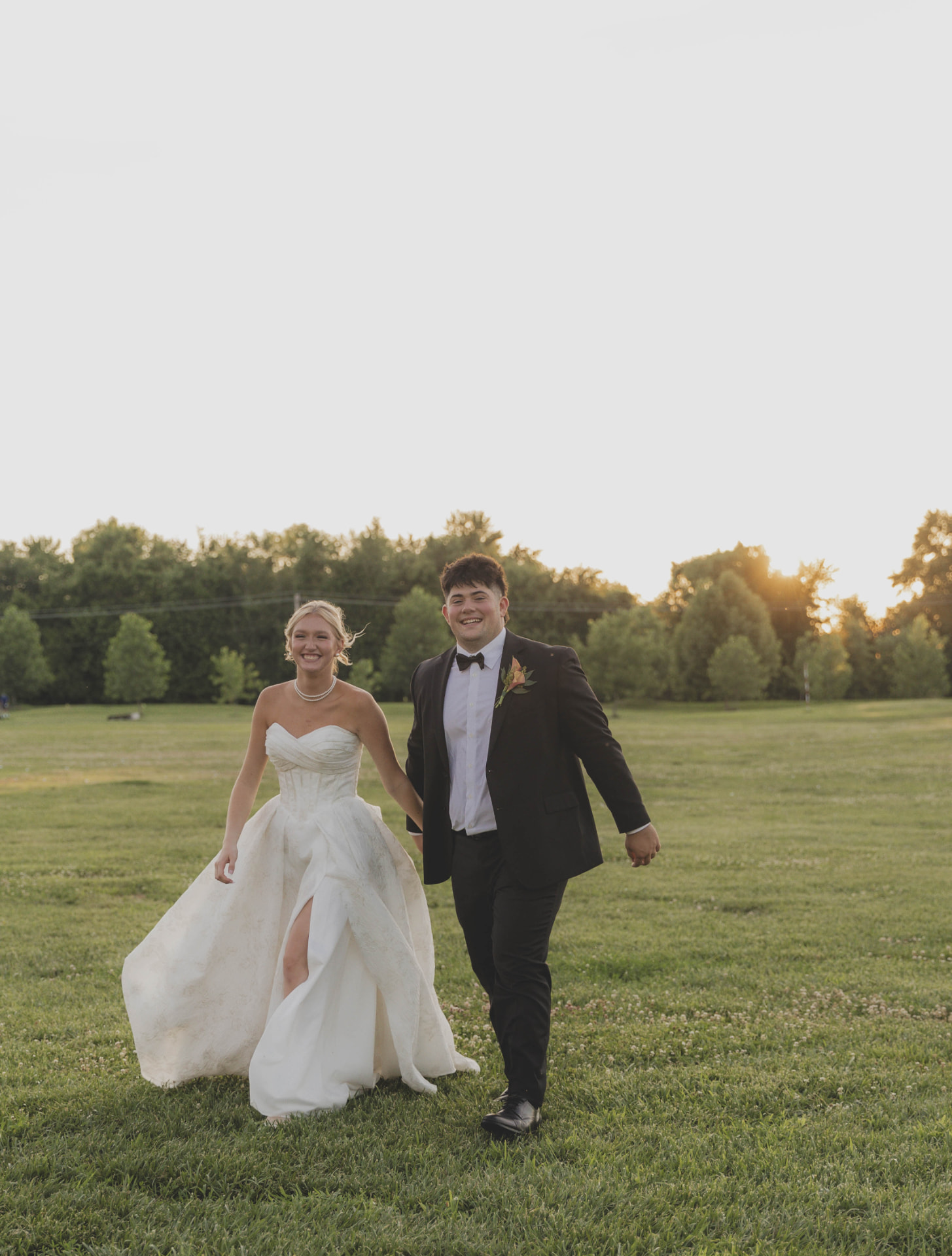 Bride and groom walking hand in hand through a golden hour field at a mid-Missouri wedding